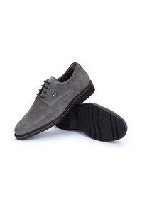 Chaussures en daim grises à lacets avec un bout arrondi et une semelle en caoutchouc noir. Présente un logo discret sur le côté et une texture lisse.