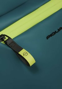 Bolsa impermeable de color verde azulado con una cremallera texturizada de neón amarillo y una lengüeta de tirador negra con un logo en relieve, que enfatiza la durabilidad y funcionalidad.