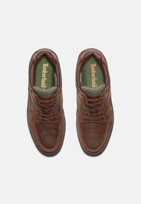 Brūni ādas apavi ar teksturētu virsmu, ar apaļ�ām auklām, mīkstu apkaklīti un zaļu iekšzoli ar Timberland logo.