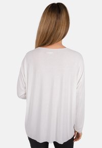 Weißes Langarmoberteil aus weichem, strukturiertem Stoff. Mit weitem Ausschnitt und abgerundetem Saum für einen lässigen Fall. Rückansicht dargestellt.