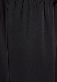 Črn material z gladko teksturo, zategnjen na vrhu z elastiko. Oblika je preprosta in ravna, z rahlimi gubami, ki so vidne.