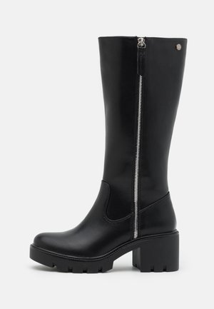 Czarny skórzany but do połowy łydki z masywnym obcasem i bocznym zamkiem błyskawicznym, z teksturowaną podeszwą i małym metalowym logo umieszczonym blisko góry.