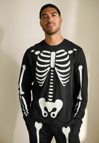 Sort langærmet skjorte med en hvid skeletgrafik på forsiden, med hvide skeletarme og ben design på ærmerne.