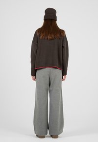 Brązowy sweter dziany z czerwonym wykończeniem w dole, w zestawieniu z szerokimi szarymi spodniami. Osoba nosząca prążkowaną brązową czapkę, widziana z tyłu.