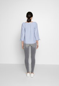 Blusa a rayas azul y blanca con cuello fruncido, mangas tres cuartos y lazos. Jeans ajustados grises y zapatillas blancas completan el look.