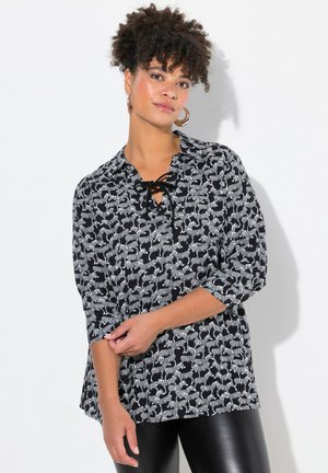 Schwarze Bluse mit einem sich wiederholenden weißen Tierdruck, V-Ausschnitt mit Schnürdetails, Dreiviertelärmel und lockerer Passform.
