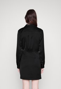 Robe en satin noir à manches longues, col et taille cintrée. Présente une texture lisse et un ourlet court, conçue pour une silhouette élégante.