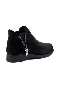 Botas de tobillo de ante negro con una suela de goma negra baja, que presentan un cierre lateral con cremallera y una textura suave. Diseño clásico con acentos mínimos.