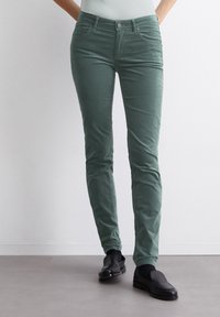 Groene corduroy broek met een slanke pasvorm, vijf zakken en een knoopsluiting, gecombineerd met zwarte instap schoenen. Gladde textuur en effen kleur.
