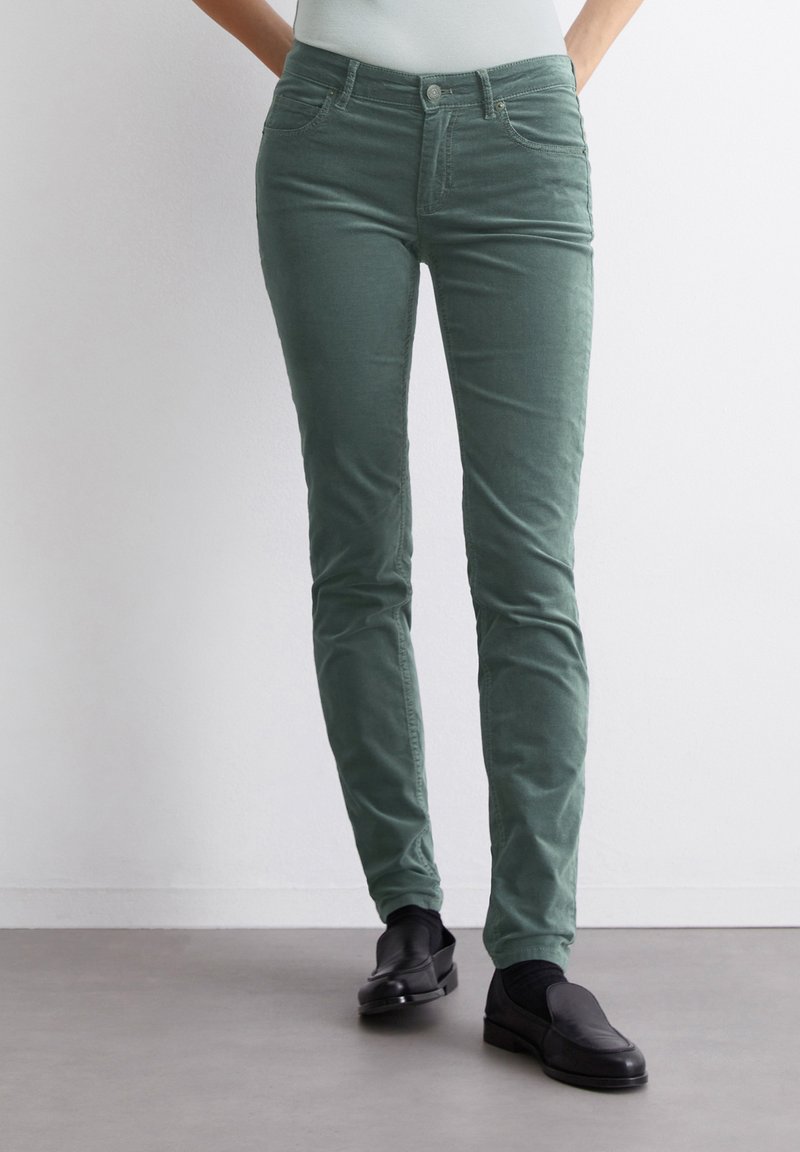 Groene corduroy broek met een slanke pasvorm, vijf zakken en een knoopsluiting, gecombineerd met zwarte instap schoenen. Gladde textuur en effen kleur.