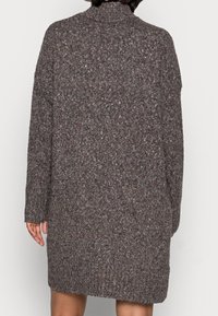 Vestito a maglione marrone con collo alto, maniche lunghe e superficie strutturata con sfumature colorate. La vista posteriore mostra una vestibilità comoda.