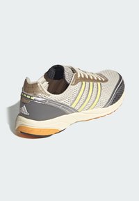 Αθλητικό παπούτσι ελαφρού βάρους με ανώτερο μέρος από αεριζόμενο δίχτυ σε γκρι και κρεμ, με κίτρινες ρίγες, επενδυμένη σόλα και υφασματικές λεπτομέρειες.