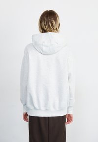 Lichtgrijze hoodie met een grote capuchon, geribde manchetten en zoom. Zachte textuur, oversized pasvorm. Achteraanzicht toont een gladde stof en een casual ontwerp.