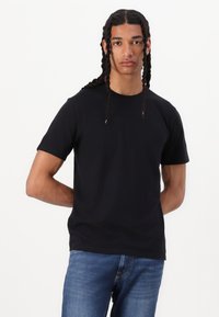 Svart t-skjorte med kort erm laget av bomull, med rund hals og en avslappet passform, stylet med blå denimjeans.