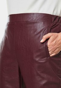 Bordeaux leren broek met een gladde textuur, hoge taille en zijzakken, met een op maat gemaakte ontwerp dat comfort en stijl combineert.