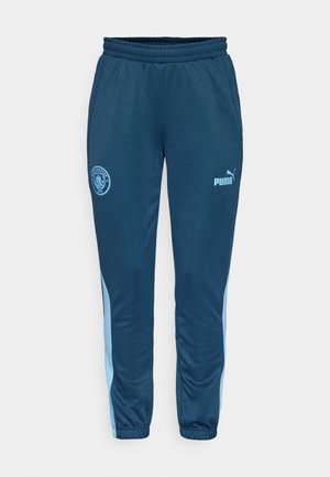 Niebieskie spodnie sportowe wykonane z gładkiego materiału, zdobione logo Manchester City oraz jasnoniebieskimi paskami po bokach. Elastyczny pas i mankiety.