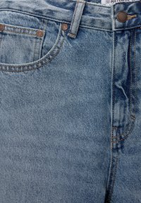 Jeans de mezclilla azul claro con una textura suave, costuras visibles, remaches de cobre y detalles en los bolsillos delanteros.