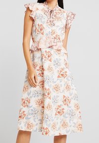 Blommig midiklänning i ljus krämfärg med rosa och blå blommönster. Har volangärmar och en figurnära bodice med peplumdetalj.