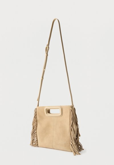 Sac bandoulière en daim beige avec une longue sangle ajustable et des franges sur les deux côtés, doté d'une poignée rectangulaire découpée sur le dessus.