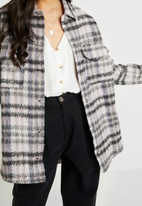 Plaid wool-blend shirt jacket in pink, gray, and black, featuring silver snap buttons and two chest pockets, layered over a white top.