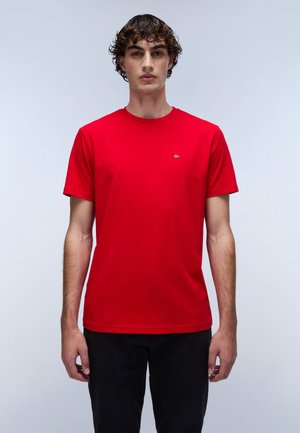 Rotes Baumwoll-T-Shirt mit Rundhalsausschnitt, kurzen Ärmeln und kleinem Logo auf der Brust; kombiniert mit schwarzen Hosen.