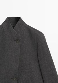 Czarny wełniany płaszcz o wysokim kołnierzu, zapinany na pojedynczy guzik, z teksturowanym materiałem zawierającym subtelne detale i czyste linie.