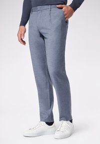 Pantaloni su misura di colore azzurro chiaro realizzati in tessuto strutturato, con pieghe stirate e tasche laterali, abbinati a sneakers bianche.