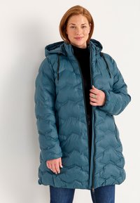 Teal pufjakke med hætte, der har et quiltet mønster og snorede detaljer. Materialet ser glansfuldt ud, med et mellemlangt design.