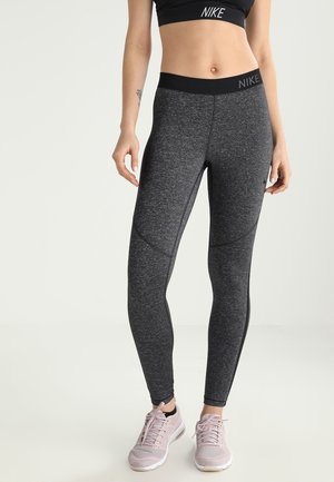 Czarne legginsy Nike o teksturowanym materiale, z wysokim stanem i bocznymi panelami. W zestawie z jasnoróżowymi butami sportowymi.
