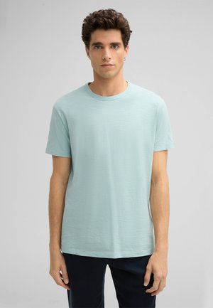 T-shirt verde chiaro a maniche corte, colletto rotondo, texture morbida, vestibilità comoda, abbinato a pantaloni scuri, design semplice, senza motivi o loghi visibili.