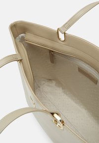 Sac à main beige avec un extérieur en cuir lisse, quincaillerie dorée et intérieur à motifs. Comprend une poche zippée et un design spacieux.