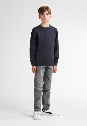 Marineblauwe trui met lange mouwen, ronde halslijn en geribbelde manchetten, gecombineerd met lichtgrijze jeans en witte sneakers met zwarte accenten.