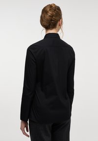 Black, long-sleeve shirt with a collar, featuring a smooth texture and clean lines. The back shows a straight cut without visible fasteners.