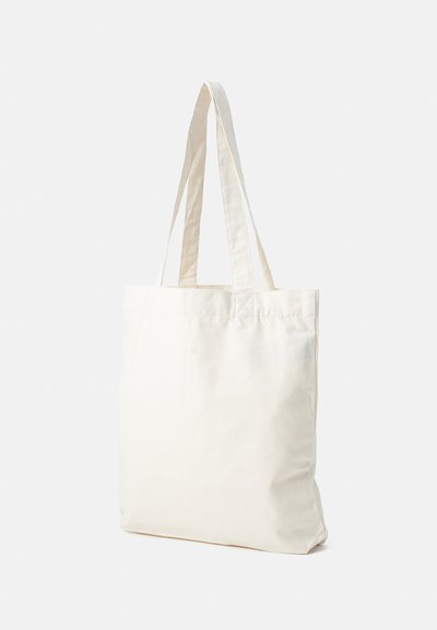 Sac de pânză de bumbac alb crem, cu două mânere, stând vertical pe un fundal deschis.