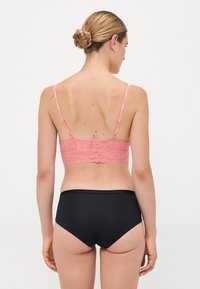 Rosa blonde bralette med bølgete kanter og justerbare stropper, kombinert med svarte høytaljede truser, som fremhever en glatt tekstur.