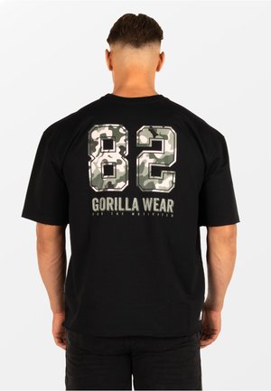 Schwarzes T-Shirt mit großen grünen Camouflage-Zahlen "82" und Markentext "GORILLA WEAR" auf der Rückseite. Kurze Ärmel und eine lockere Passform.