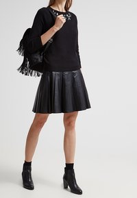 Czarny dzianinowy sweter z kwiatowymi zdobieniami, połączony z czarną plisowaną skórzaną spódnicą, czarnymi botkami na kostkę i frędzlowym czarnym plecakiem.