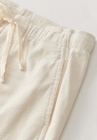Gros plan sur un pantalon en tissu côtelé de couleur crème avec ceinture élastique et cordon de serrage.