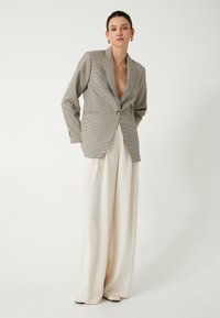 Blazer a motivo pied de poule in grigio e nero con chiusura a un bottone. Abbinato a pantaloni a gamba larga color crema. Texture morbide.