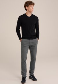 Pulover negru, strâmt, cu mânecă lungă și gât în V, asortat cu pantaloni gri slim-fit, completat cu adidași negri cu dungi albe.