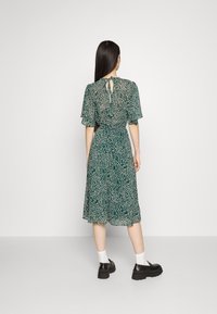 Vihreä kukkamekko, jossa on lyhyet, röyhelöiset hihat, tiukka vartalo ja levenevä hame. Sisältää avattavan selkädetailin ja kevyen kankaan.