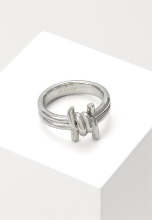 Bague en argent avec un détail de conception en fil barbelé sur une bande lisse, présentée sur un support géométrique blanc.