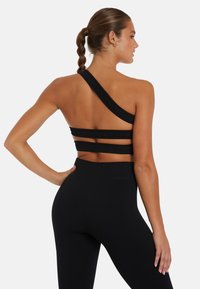 Zwarte geribde sporttop met één schouderband, voorzien van drie horizontale bandaccenten op de rug. Gecombineerd met high-waisted zwarte leggings.