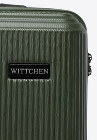 Tvrdý tmavě zelený kufr s vertikálními drážkami a černou etiketou se nápisem "WITTCHEN" na přední straně.