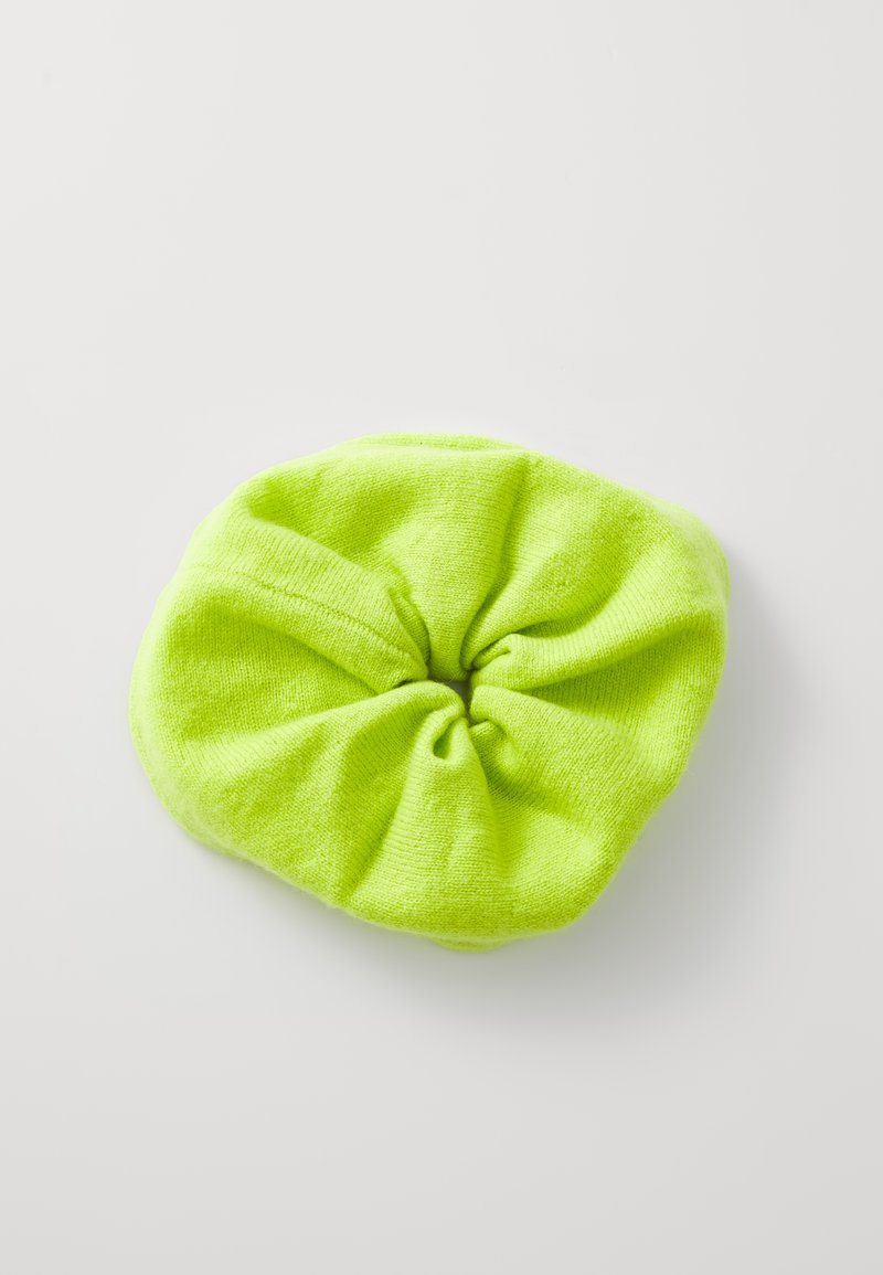 Neon groene stof scrunchie met een zachte textuur en verzameld ontwerp, met een centrale knoop. De vorm is rond en elastisch.