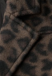 Lederimitatstoff mit Leopardenmuster und einer weichen, flauschigen Textur. Dominierende Farben sind Dunkelbraun, Schwarz und ein helleres Beige, die ein kontrastierendes Muster bilden.