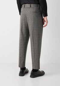 Graue Karohosen mit entspannter Passform, Gürtelschlaufen und Seitentaschen, kombiniert mit schwarzen Lederschuhen und schwarzen Socken.