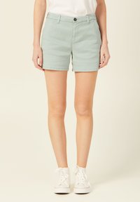 Shorts en coton vert clair avec une coupe droite, ceinture avec un bouton et poches latérales. Associés à des baskets montantes blanches.