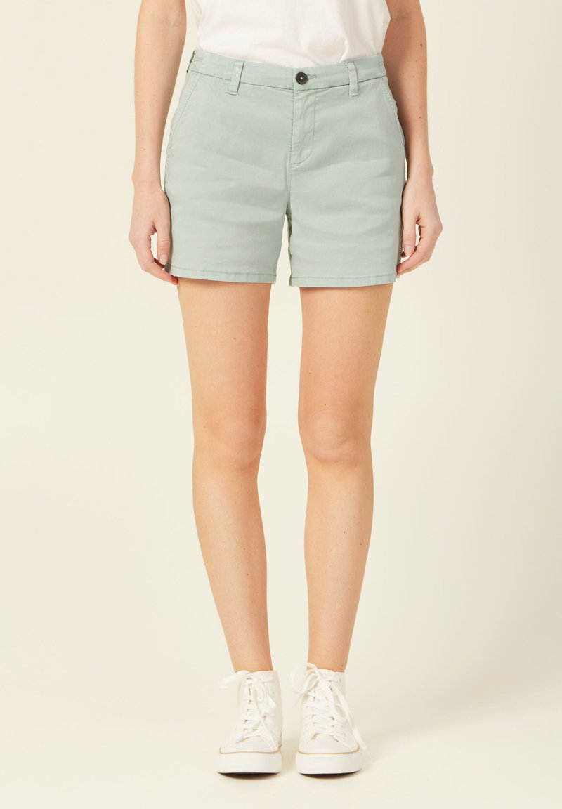 Shorts en coton vert clair avec une coupe droite, ceinture avec un bouton et poches latérales. Associés à des baskets montantes blanches.
