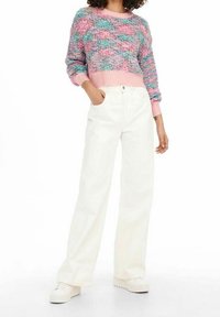 Pull à rayures multicolores avec des accents roses, col rond et manches longues, assorti à un pantalon blanc à jambes larges et des baskets blanches à plateforme.